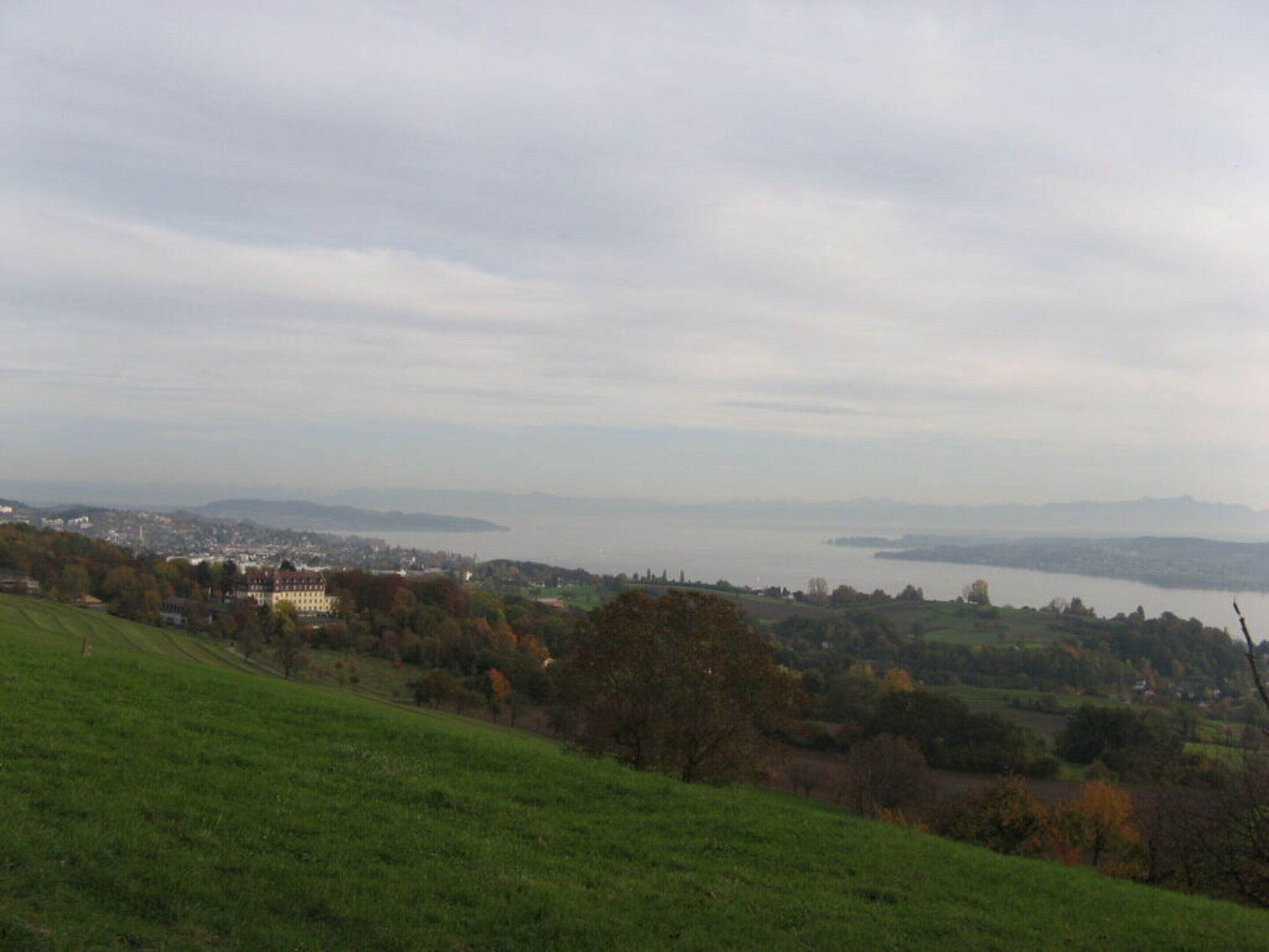 Ein weitreichender Blick auf eine Küstenstadt mit einem markanten Gebäude auf einem Hügel, einem Gewässer und sanften Hügeln.