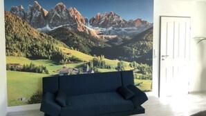 Una habitación con un gran mural de paisaje montañoso, un sofá azul oscuro y una puerta blanca.