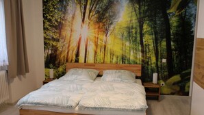 Un dormitorio con una cama de madera, un mural temático de bosque y una mesita de noche con una lámpara.