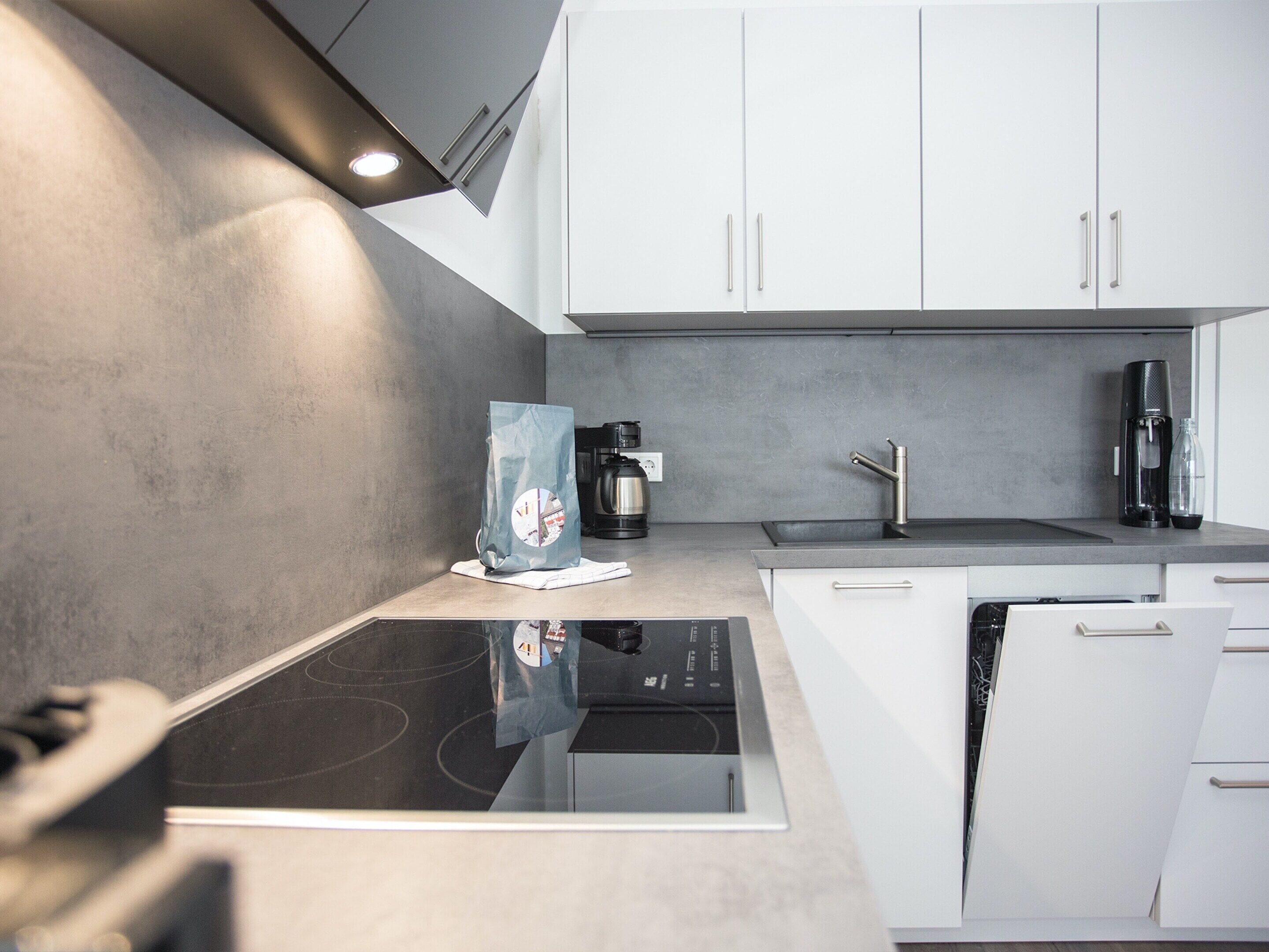 A modern kitchen with white cabinets, a built-in stove, and a coffee maker.