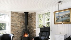 A cozy room with a stone wall, a black wood-burning stove, a black leather chair, and a white cabinet with a painting.