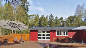 A red cabin with a deck, outdoor seating, and a large umbrella.
