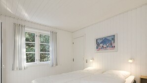 A bedroom with a bed, a window with curtains, a door, and a wall-mounted light fixture.