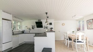 A modern kitchen with white cabinetry, a black countertop, and a central island. There is a dining area with a wooden table and white chairs.