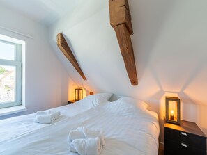 Un dormitorio con una cama grande, vigas de madera, dos mesitas de noche con lámparas y una ventana.