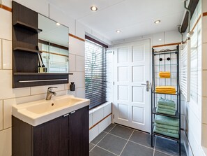 A modern bathroom with a white sink, dark wood cabinets, a glass shower enclosure, and a towel rack with yellow and green towels. - Cosy Holiday Flat 'bolle Bet' Near Beach (Tuitjenhorn)