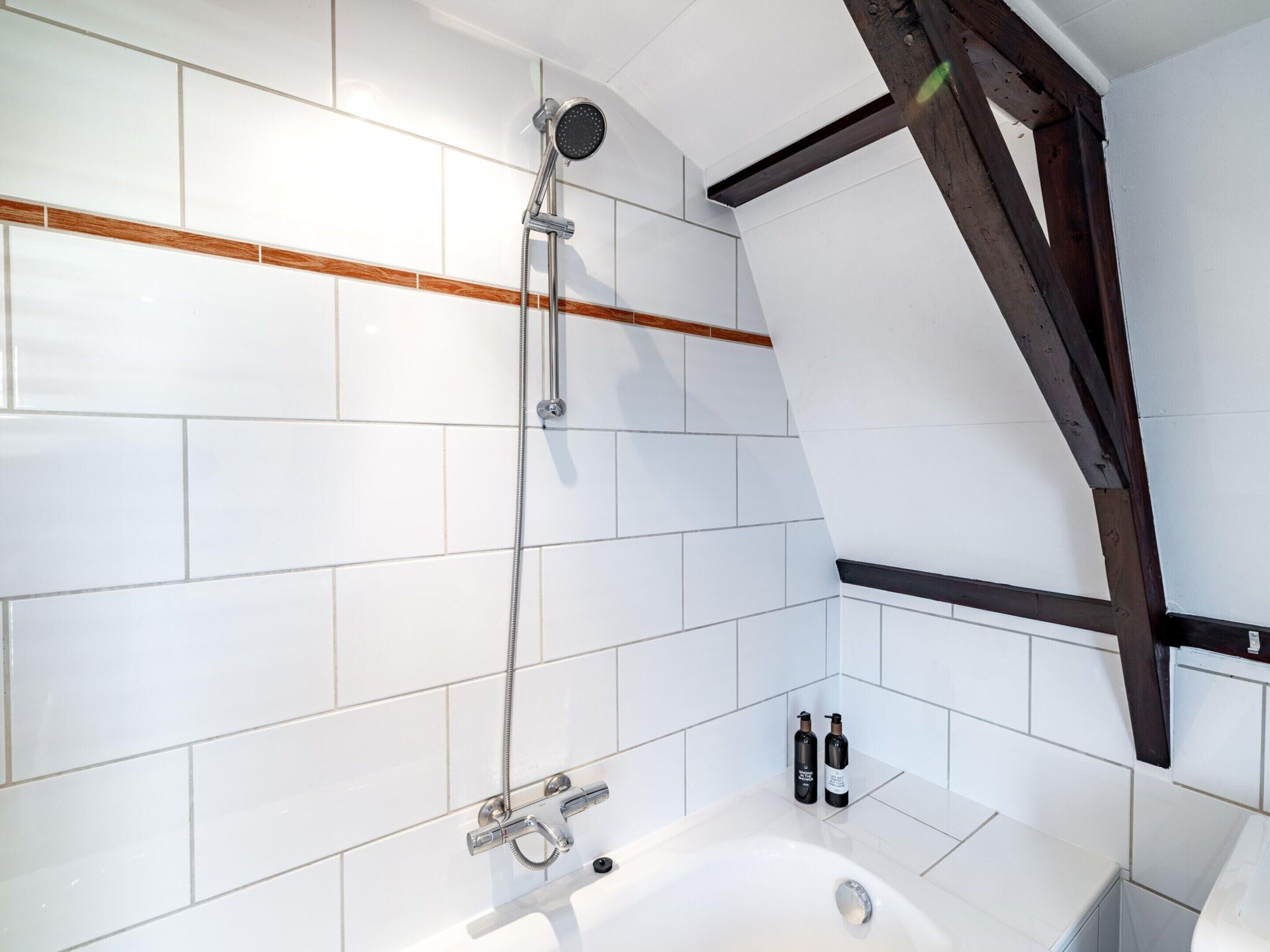 A modern bathroom with white tiles, a bathtub, a showerhead, and two bottles of shampoo.