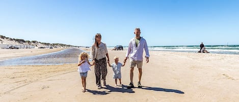A family walking on a sandy beach with a clear sky.