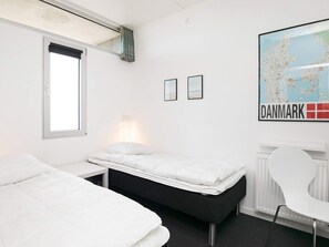 A minimalist hotel room with a bed, a desk, and a chair. There's a map of Denmark on the wall.