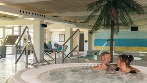 A hot tub area with a palm tree, lounge chairs, and a tiled floor.