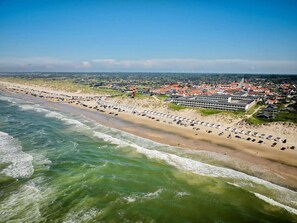 An aerial view of a coastal area with a beach lined with beach huts and a row of houses.