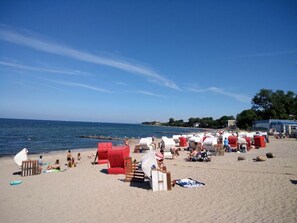 Una playa con hileras de sillas y sombrillas rojas y blancas, una orilla arenosa y el mar al fondo.