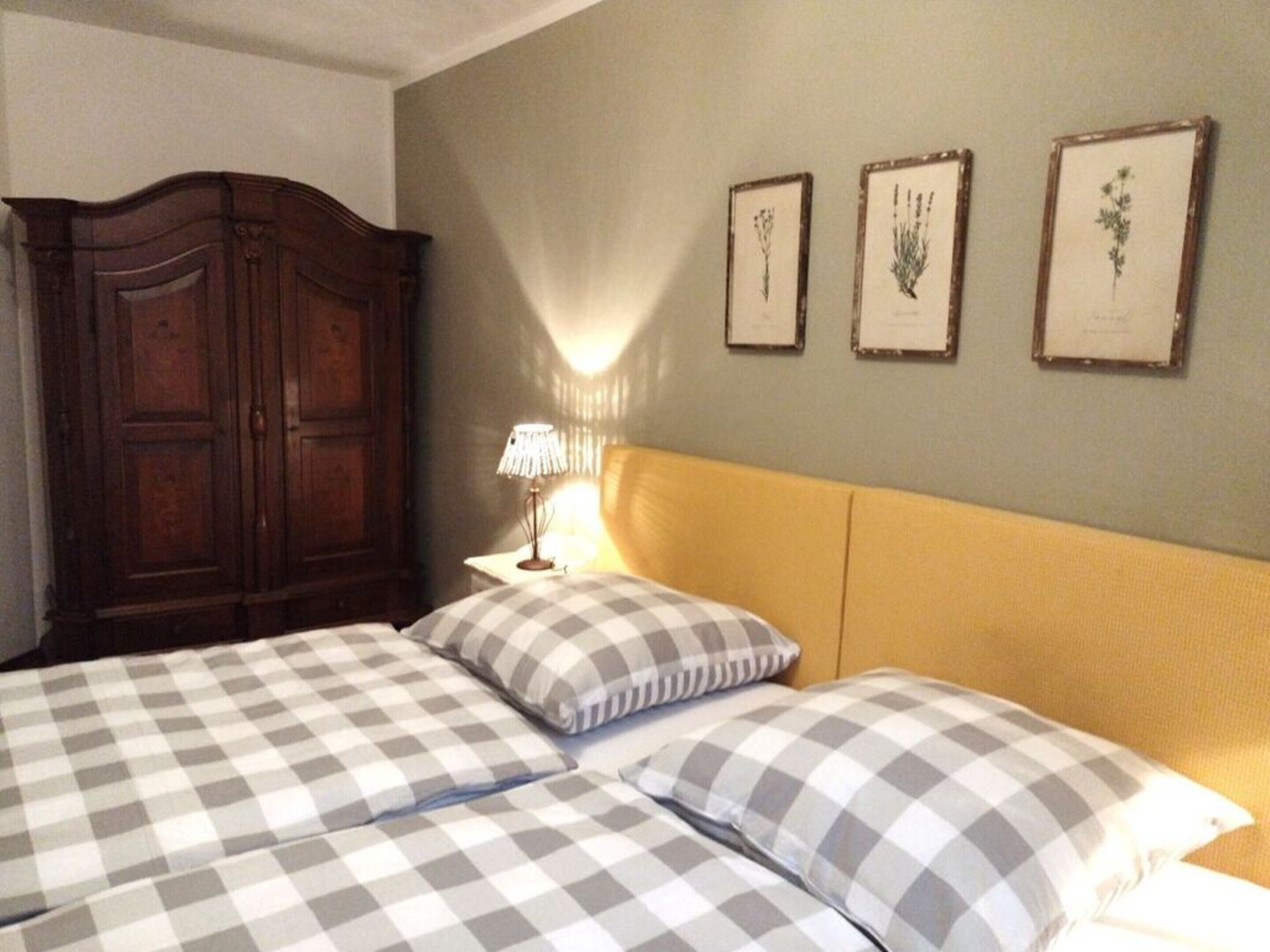 A bedroom with two beds, a wooden wardrobe, and three framed botanical prints on the wall.