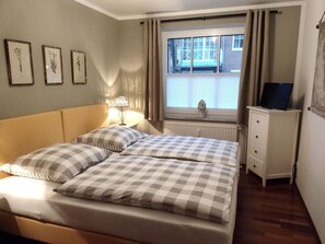 Un dormitorio con cama, mesita de noche, cómoda y ventana con cortinas.