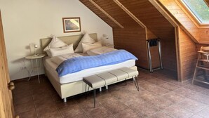 Ein Schlafzimmer mit schrägem Dach, einem Bett mit blauer Decke, einem Nachttisch mit Lampe und einem kleinen Fenster.
