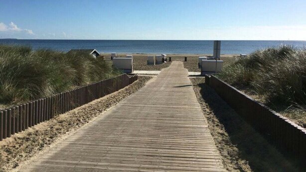 A wooden boardwalk leading to beach huts, surrounded by dunes. - Time out Karlshagen Comfortable Vacation Home (Karlshagen)