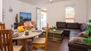 A cozy living room with a dining area, a sofa, and a television displaying a scenic view. - Time out Karlshagen Comfortable Vacation Home (Karlshagen)