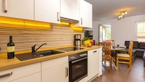 A modern kitchen with white cabinets, a wooden countertop, a built-in oven, and a dining area with a table and chairs. - Time out Karlshagen Comfortable Vacation Home (Karlshagen)
