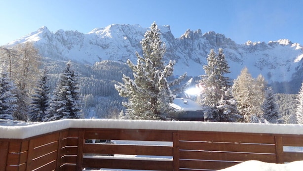 Un balcon en bois offrant une vue sur des montagnes et des arbres enneigés.