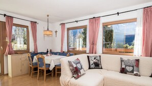 Un salon chaleureux avec un grand canapé d’angle beige, une table à manger avec des chaises et une vue sur l’extérieur grâce à de grandes fenêtres.