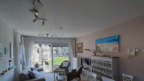 A modern living room with a sofa, dining table, and chairs. There is a TV, a phone, and a painting on the wall. - De Haan Comfortable Holiday Residence (De Haan)