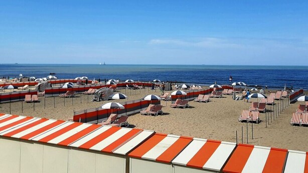 A beach with striped umbrellas and lounge chairs, a clear sky, and the ocean in the background. - De Haan Comfortable Holiday Residence (De Haan)
