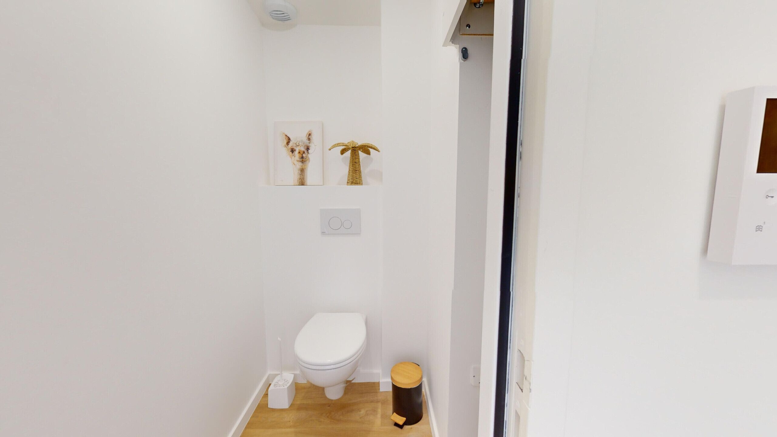 A small, clean bathroom with a toilet, a small trash bin, and two wall-mounted decorative items.