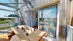 Un terrazzo in legno con tavolo e sedie, una porta vetrata che dà su un balcone e un ombrellone colorato.