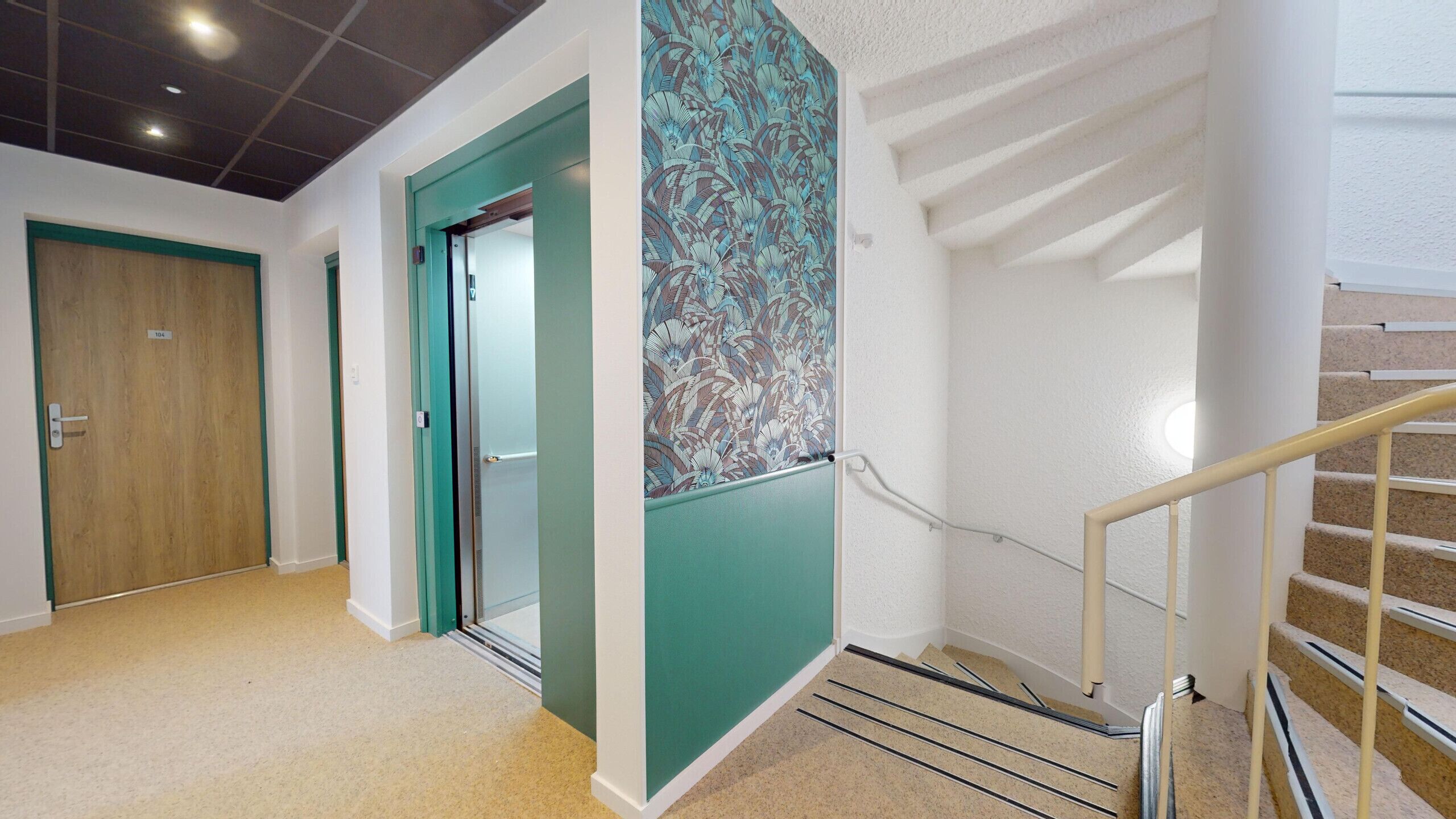 A hallway with a wooden door, a green door, and a staircase with a metal railing.