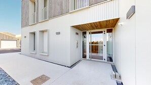 Un edificio moderno con facciata bianca, ampie porte in vetro e tetto a lamelle di legno sopra l'ingresso.