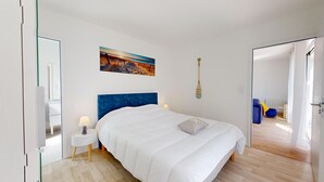 Una camera da letto con un letto grande, un dipinto raffigurante una spiaggia, un remo di legno e vista su una sedia blu e un termosifone attraverso una porta aperta.