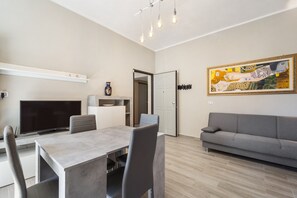 Uma sala de estar moderna com área de jantar, um sofá cinza, televisão de tela plana e um quadro na parede.