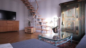 A living room with a wooden TV stand, a glass coffee table, a decorative cabinet, and a spiral staircase. - Holiday Apartment 2 Oldenbug (Oldenburg)