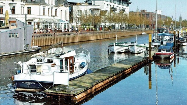 A calm waterway with a docked boat named 'OLDENBURG OYC' and other boats. There are buildings and trees along the shore. - Holiday Apartment 2 Oldenbug (Oldenburg)