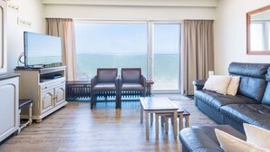 A modern living room with a large window, a flat-screen TV, a sofa, and a coffee table. - Apartment With sun Facing Terrace (Middelkerke)
