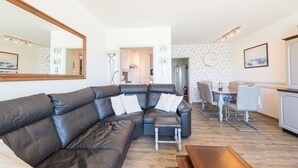 A modern living room with a leather sectional sofa, a wooden coffee table, and a dining area with a table and chairs. - Apartment With sun Facing Terrace (Middelkerke)