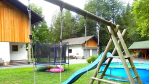 Un ensemble de jeux en bois comprenant une balançoire, un trampoline et un toboggan, installé dans un jardin avec une piscine.