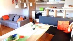 Un salon moderne avec un canapé gris, une table basse en bois et une cuisine en arrière-plan.