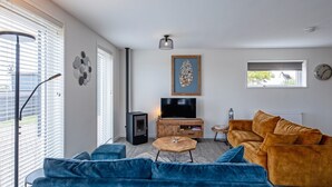 A modern living room with a blue sofa, a wooden coffee table, and a television on a wooden stand. - Holiday Home Near Forest With Wellness Garden (Den Burg)