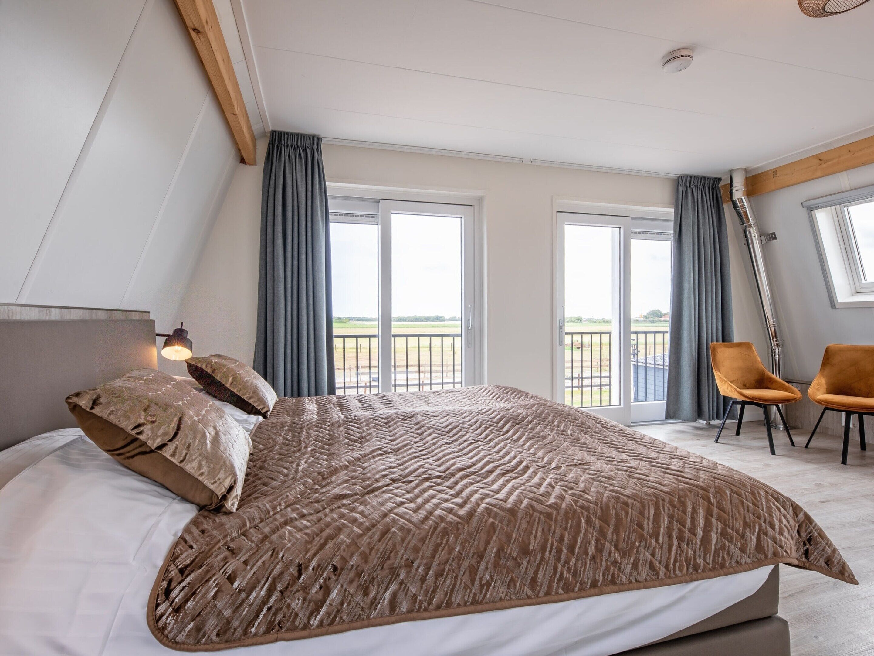 A bedroom with a large bed, two chairs, and a balcony with a view.