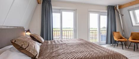 A bedroom with a large bed, two chairs, and a balcony with a view.