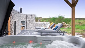 A hot tub with two lounge chairs, a stone wall, and a wooden pergola. - Holiday Home Near Forest With Wellness Garden (Den Burg)