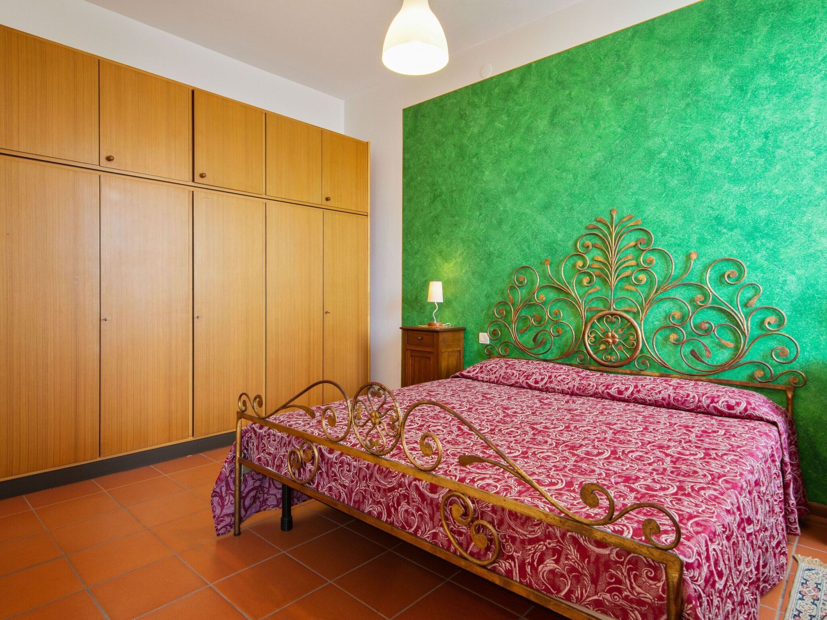 A bedroom with a bed, wooden wardrobe, green wall, and tiled floor.