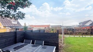 A patio with a table and chairs, surrounded by a wooden deck and a black fence.