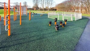 A playground with various equipment including a climbing frame, swings, and a fenced area.