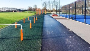 A playground with various exercise equipment, a picnic table, and a fenced area with a blue surface.