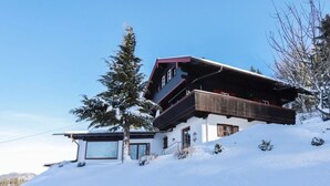 Un chalet moderne doté d’un grand balcon, situé sur une pente enneigée.