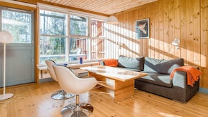 Interior acogedor de una cabaña con techo de madera, un sofá, una mesa de comedor y una silla.