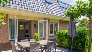 An outdoor patio with a table and chairs, a potted plant, and a hedge. - Holiday Home in Noordwijk Near the Beach (Noordwijk)