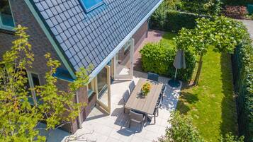 Et moderne hus med et tegltag, en terrasse med et bord og stole samt en velplejet have.
